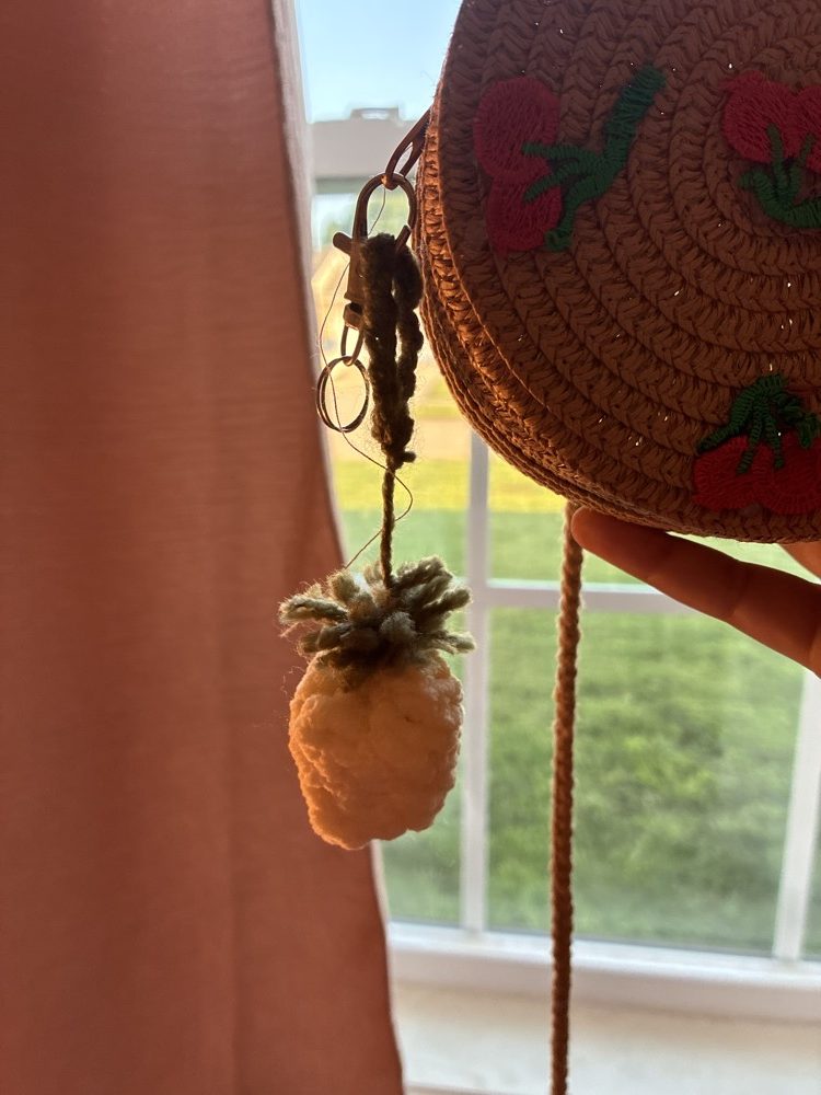 Cream crochet pineapple charm clipped to a straw bag
