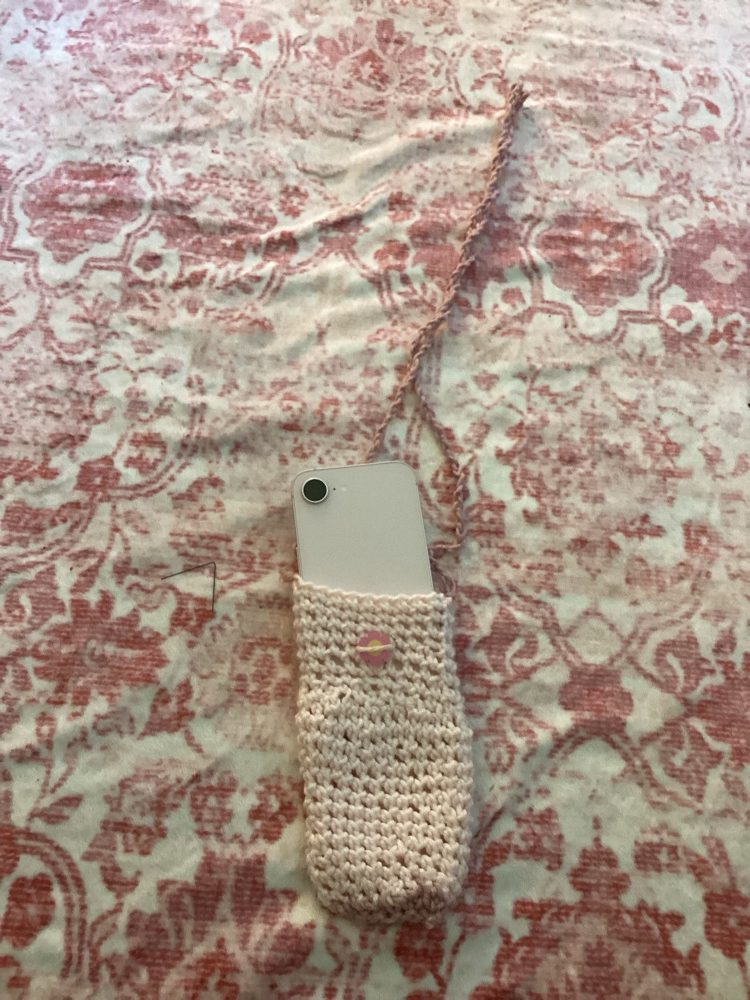 Phone peeking out of a pale pink crochet phone bag